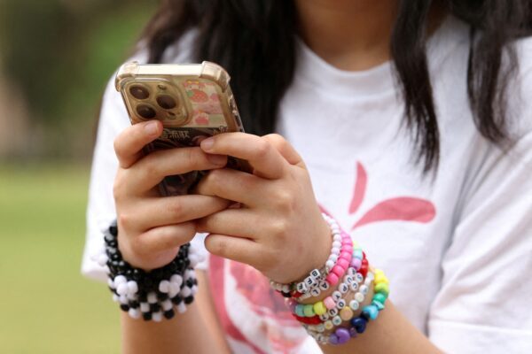 Jovem usa o celular em Sidney, na Austrália; país aprovou lei que proíbe acesso de menores de 16 anos às redes sociais — Foto: Hollie Adams/Reuters